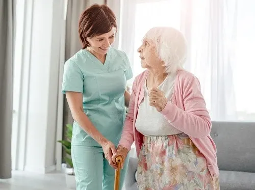 A carer helping an older woman walk with her stick