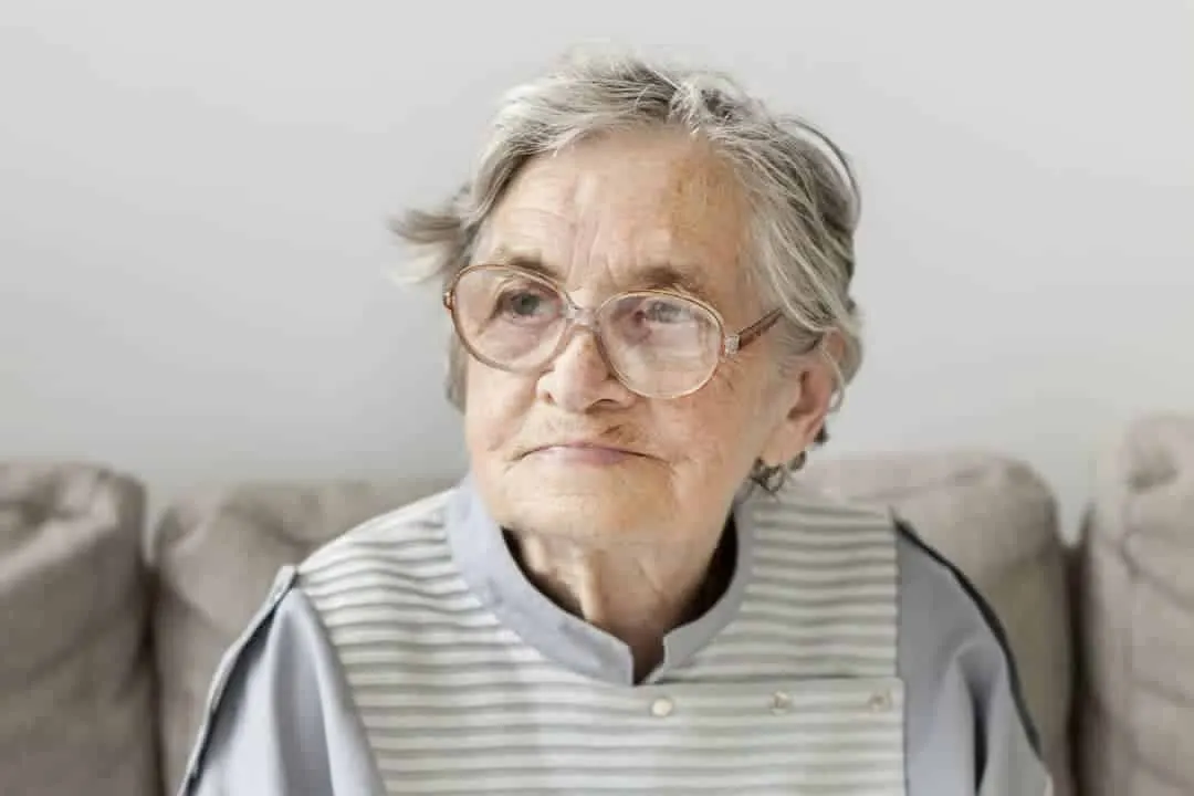 An older woman sitting on a couch, holding a walking stick